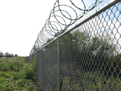 Razor wires are installed at the top of chain link fencing in the farmland.