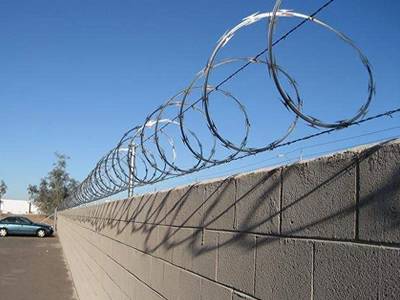 A line of single razor wire is installed on the parking lot wall.