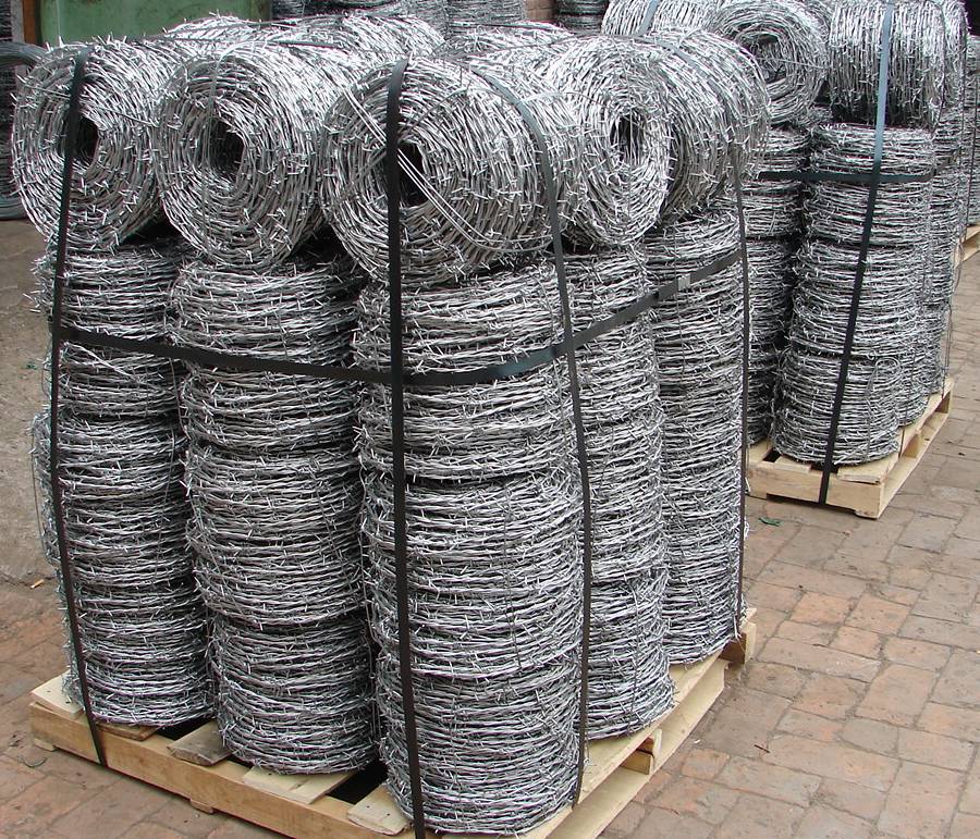 Many coils of galvanized barbed wire is packed with bailing strip on wooden pallet in workshop.