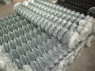 Many rolls of galvanized chain link fence with tops are packed in plastic films.