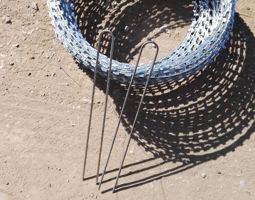 Two ground locking pegs are leaning a roll of concertina razor wire.